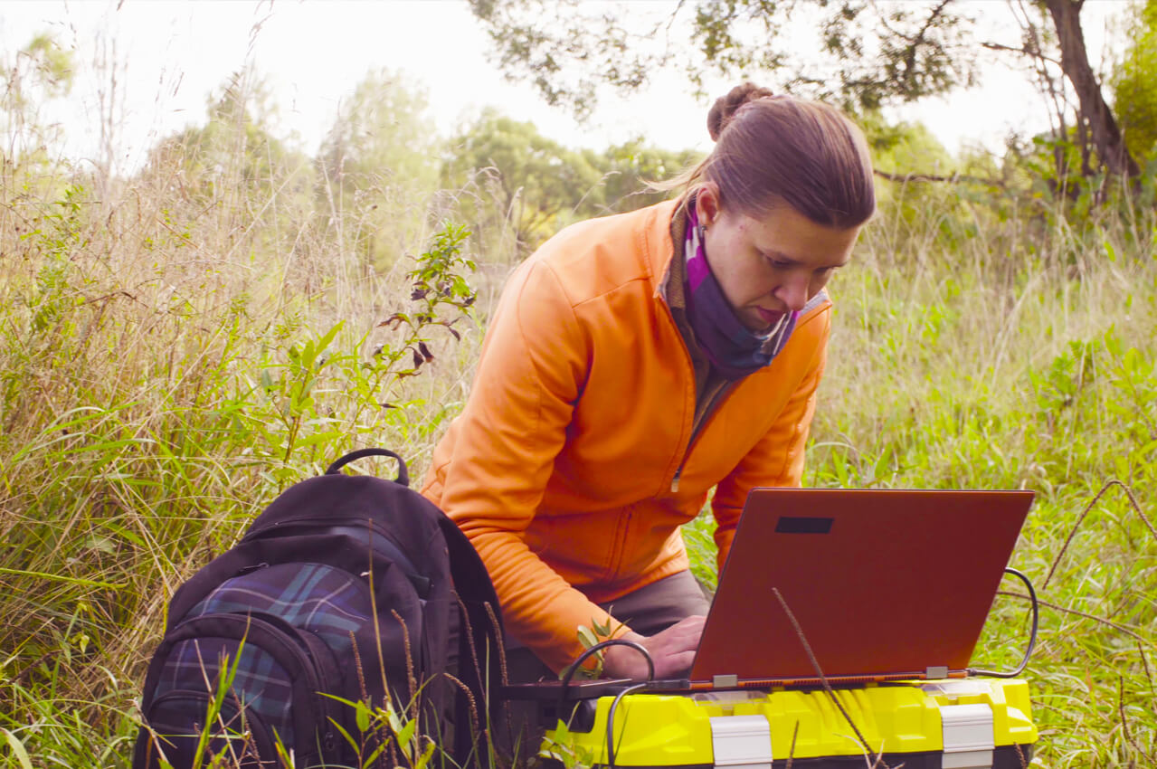 woman with laptop and backpack in a field doing research